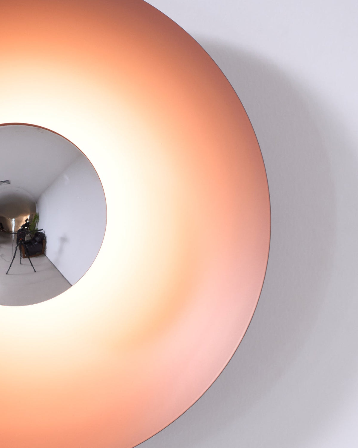 Close crop of a dusty-rose Clérachic wall light glowing warm, its mirrored centre reflecting camera gear.
