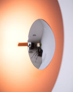 Extreme close-up of the mirrored centre on this dusty-rose Clérachic wall light, glowing warm around the edges.