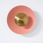 A dusty-rose Clérachic wall light on a plain white wall, its antique copper centre unlit and matte.