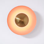 This dusty-rose Clérachic wall light glows warm on a plain wall, its antique copper centre bright at its core.