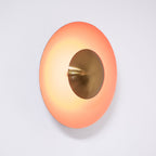 This orange Clérachic wall light glows on a wall, its antique copper centre set deep within the shade.
