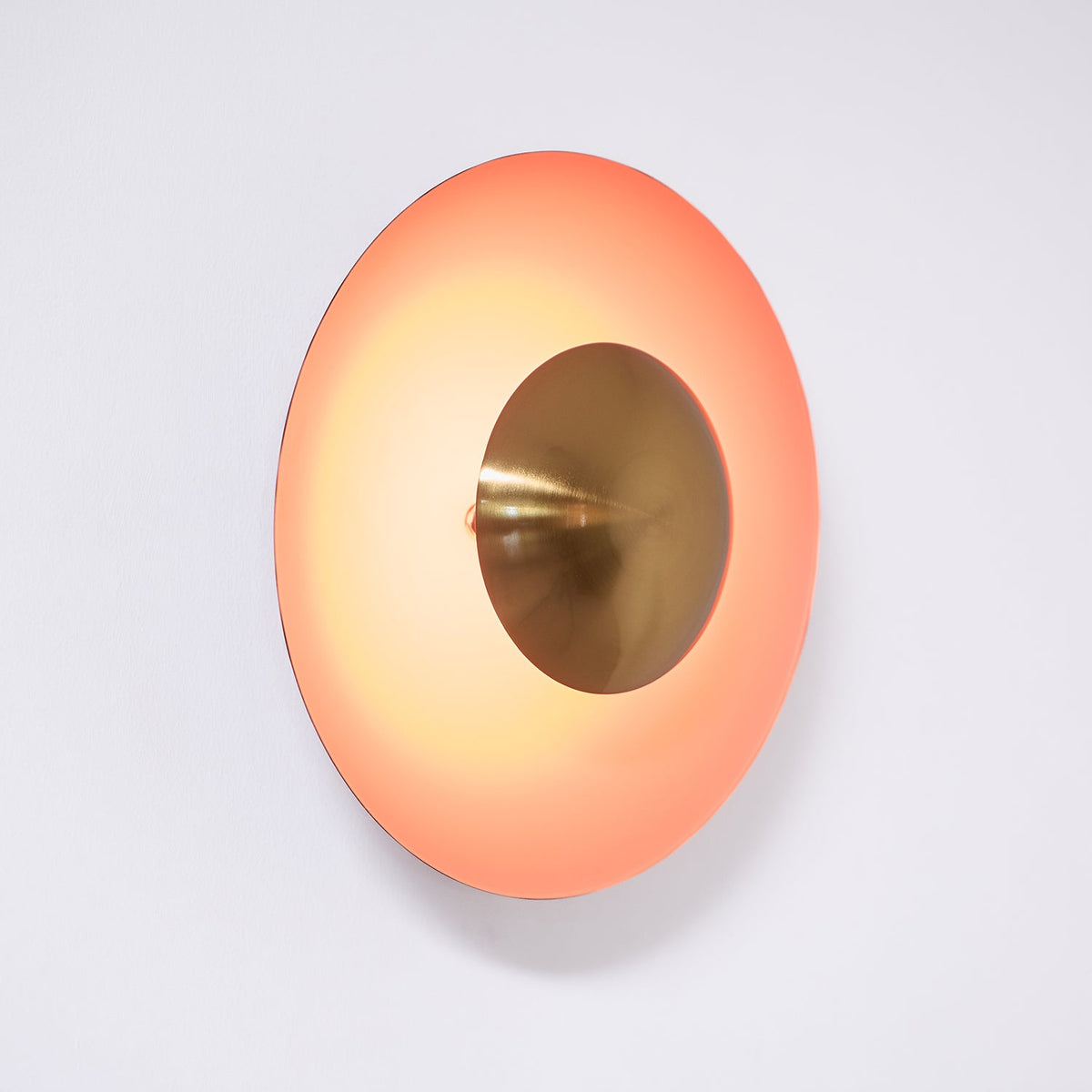 This orange Clérachic wall light glows on a wall, its antique copper centre set deep within the shade.