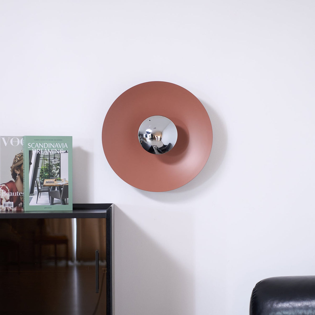A small dusty-pink Clérachic wall light above a dark cabinet, its mirrored centre catching the light.