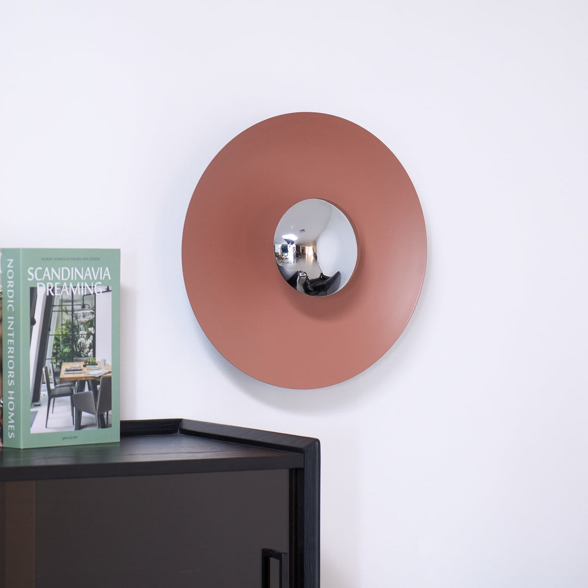 Closer view of the unlit terracotta wall light from Clérachic, its chrome centre catching daylight above a dark cabinet.