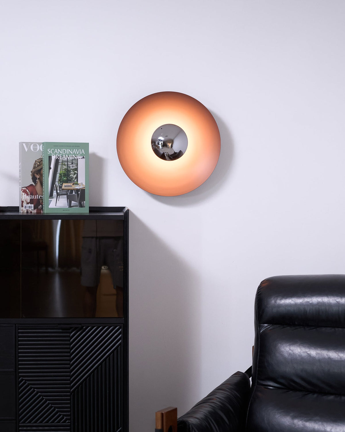 Wider view of this orange Clérachic wall light glowing above a dark cabinet, its chrome centre visible from across the room.