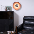 An orange Clérachic wall light glows on a white wall above a black cabinet, its chrome centre bright against the shade.