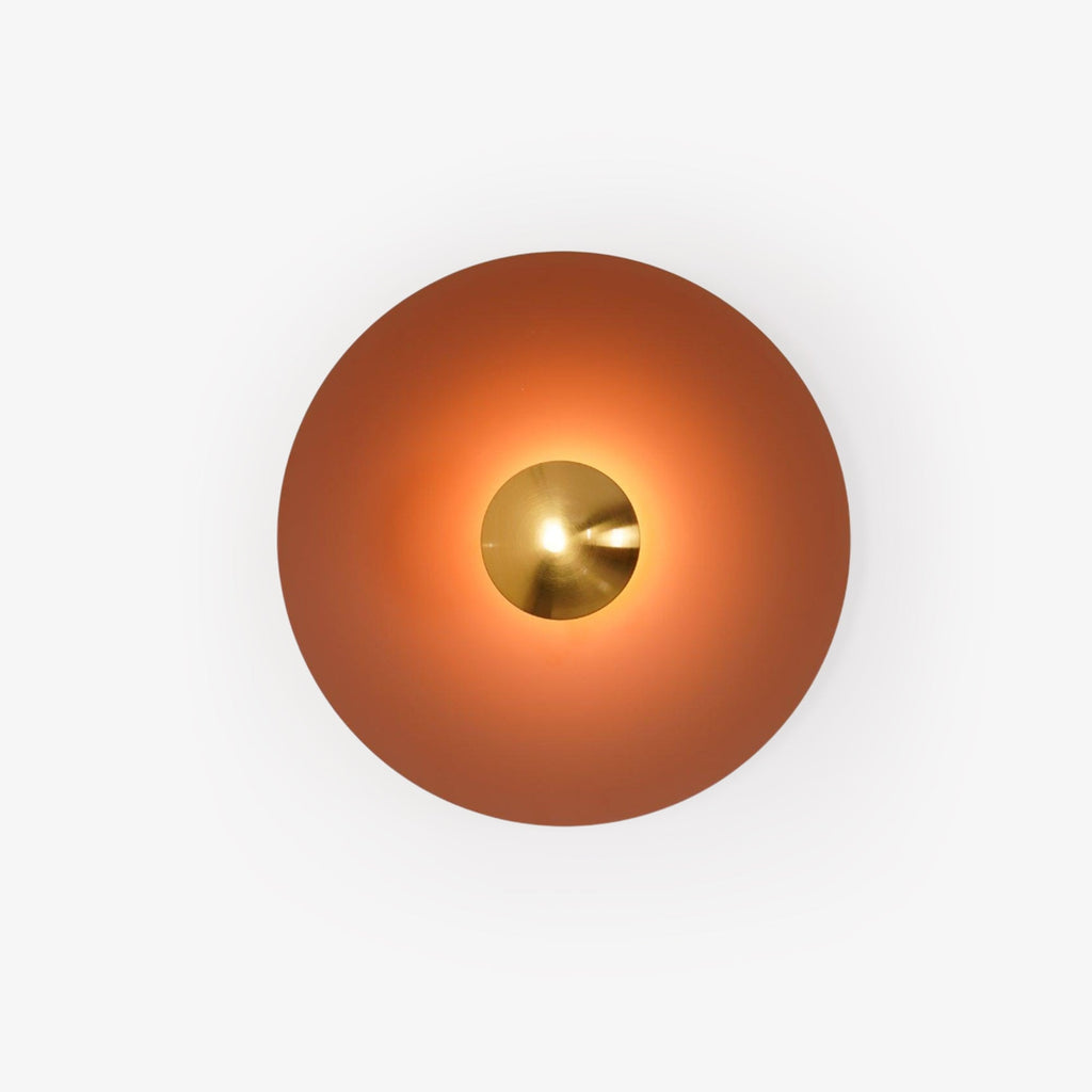 This terracotta Clérachic wall light glows warm on a plain backdrop, its brass centre bright at its core.