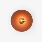 This terracotta Clérachic wall light glows warm on a plain backdrop, its brass centre bright at its core.