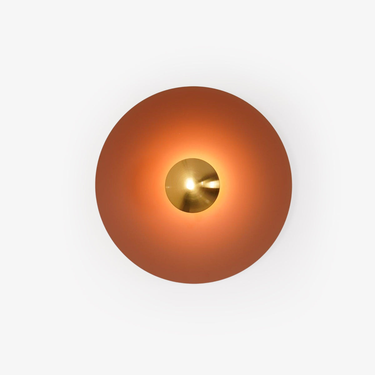 This terracotta Clérachic wall light glows warm on a plain backdrop, its brass centre bright at its core.