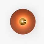 This terracotta Clérachic wall light glows warm on a plain backdrop, its brass centre lit from within.