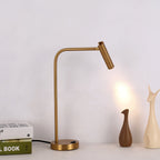 Two sculptural vases and a stack of books sit near this gold Clérachic table lamp, lit, on a shelf.