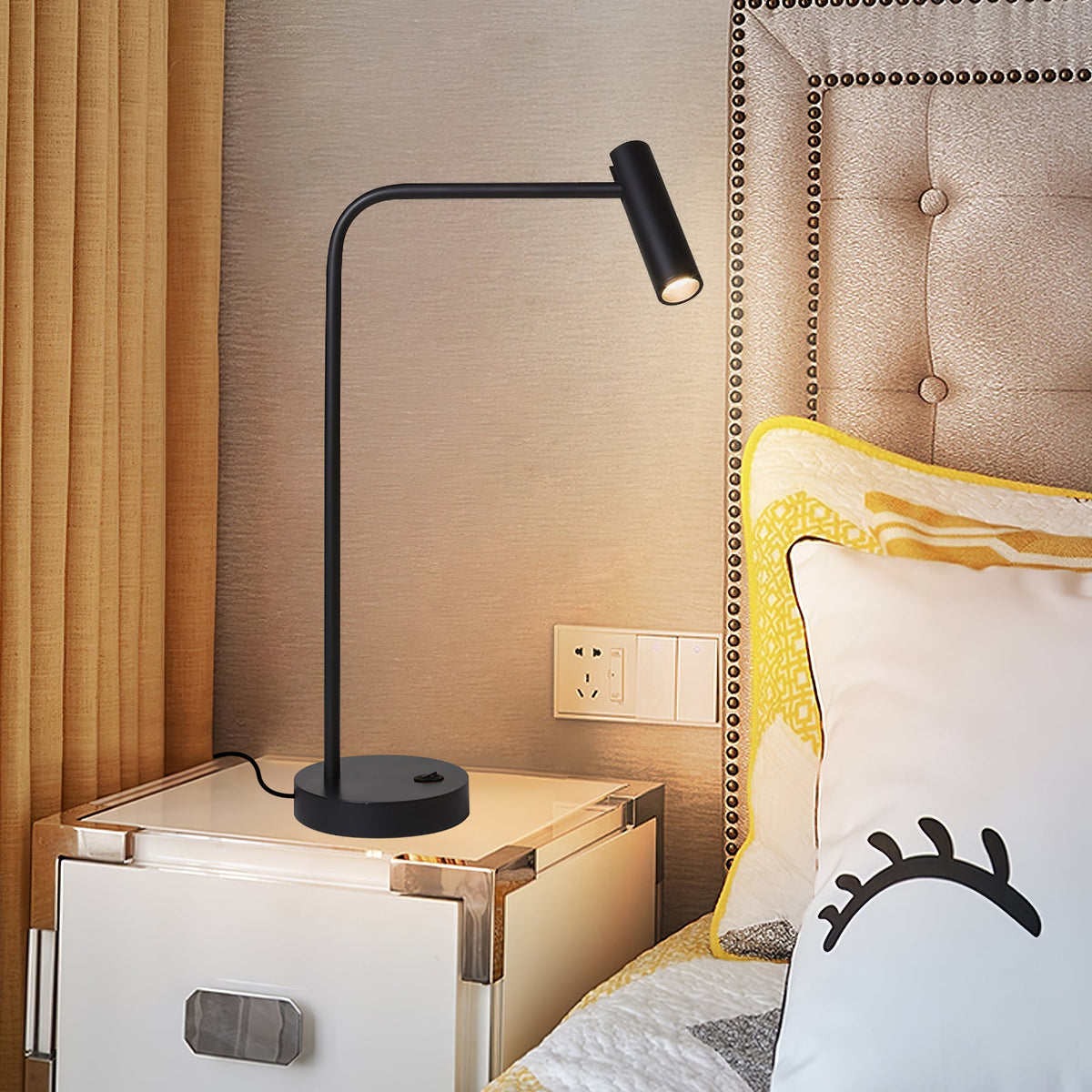A tufted headboard rises behind this black Clérachic table lamp, lit, on a white nightstand.
