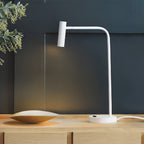 This white Clérachic table lamp glows softly on a wood sideboard against a dark teal wall.
