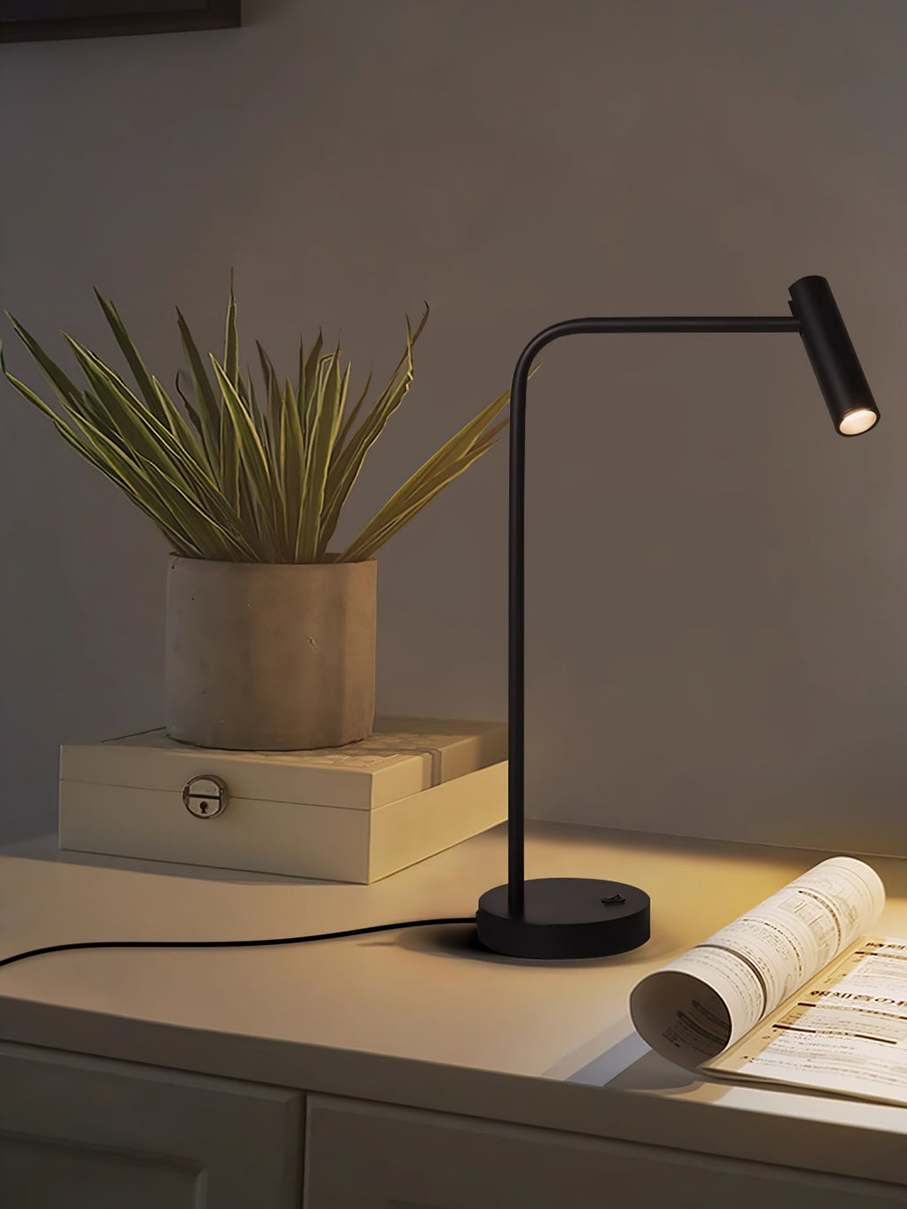 A small potted plant sits beside this black Clérachic table lamp, lit, on a pale console.