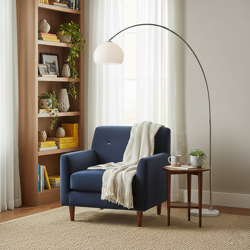 Clérachic arc floor lamp arching over a navy blue armchair with a white throw and a small wooden side table.