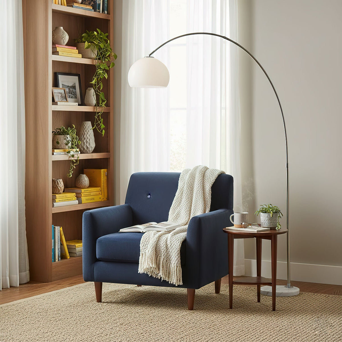 Clérachic arc floor lamp arching over a navy blue armchair with a white throw and a small wooden side table.