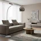 In a sheer-curtained living room, the Clérachic arc floor lamp's chrome dome shade curves above a grey sofa and coffee table.