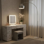In a bedroom, the Clérachic arc floor lamp's chrome dome shade stands positioned behind a lit marble vanity mirror and an orchid.