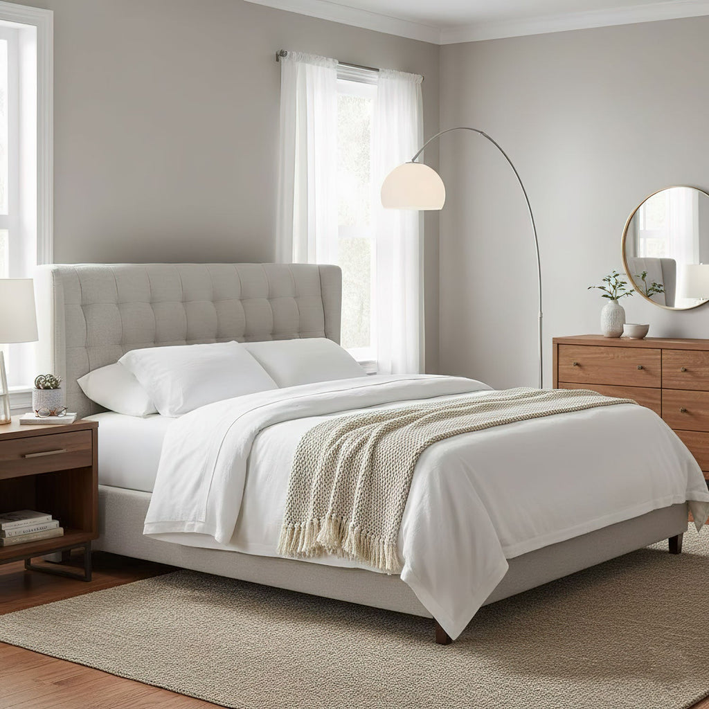 Clérachic arc floor lamp curving over a grey upholstered bed with white bedding, its marble base on the bedroom floor.