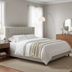 Clérachic arc floor lamp curving over a grey upholstered bed with white bedding, its marble base on the bedroom floor.