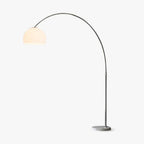 A single stainless steel arc curves from a round marble base to a glowing white dome shade on this Clérachic floor lamp, lit warm on a plain studio backdrop.
