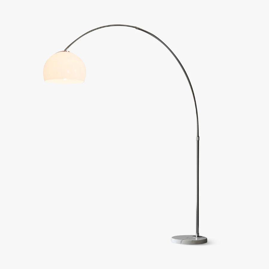 A single stainless steel arc curves from a round marble base to a glowing white dome shade on this Clérachic floor lamp, lit warm on a plain studio backdrop.