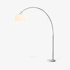 Seen at a slight angle with its cord trailing from the round marble base, this Clérachic arc floor lamp carries a plain white dome shade on steel.