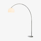 The slender steel arch of this Clérachic floor lamp rises straight from a round marble plinth to a matte white dome shade, shown unlit on white.