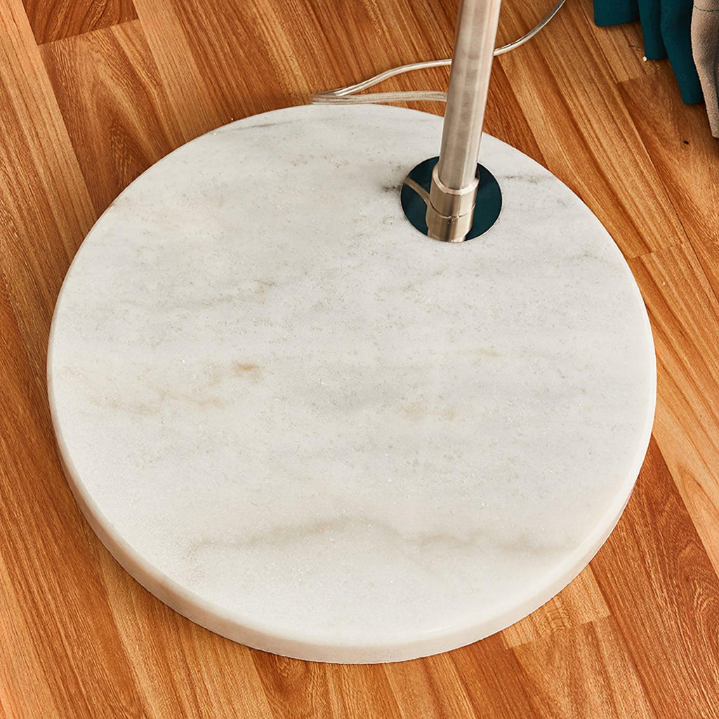 Close-up of the Clérachic arc floor lamp's round white marble base and chrome pole fitting on a wooden floor.
