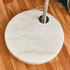 Close-up of the Clérachic arc floor lamp's round white marble base and chrome pole fitting on a wooden floor.
