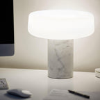 White marble Clérachic table lamp lit on a white office desk beside a computer monitor, a mouse and a pen.