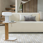 Compact white Clérachic table lamp on a round wood-and-white side table beside a cream sofa, a staircase behind.