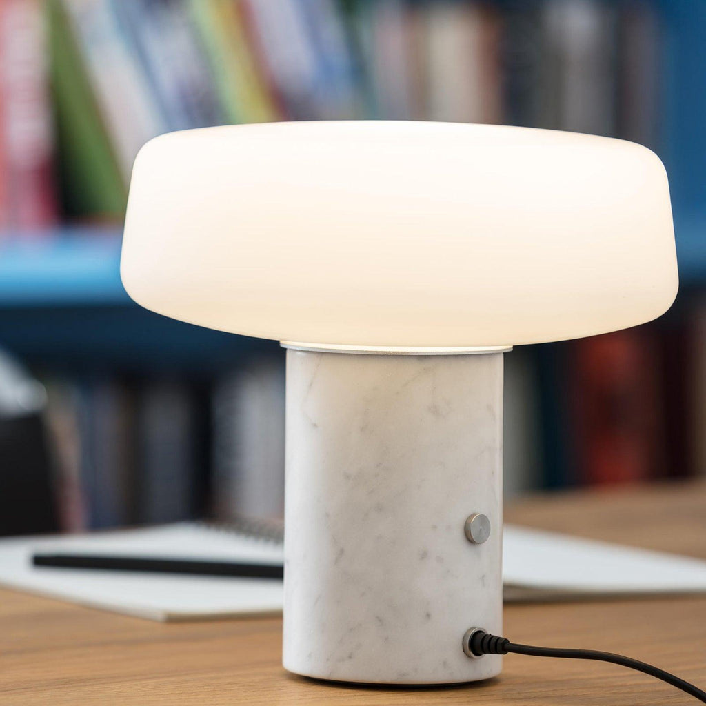 A notebook and remote sit near a dark blue bookshelf, lit by a white marble Clérachic table lamp on the desk.