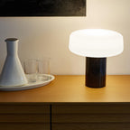 A ceramic carafe and two glasses sit on a tray beside a black marble Clérachic table lamp lit on the sideboard.