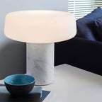 A teal bowl and stacked books rest below a white marble Clérachic table lamp lit beside a navy sofa.