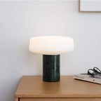 Green marble Clérachic table lamp lit on a wooden dresser corner, reading glasses resting on a stack of books.