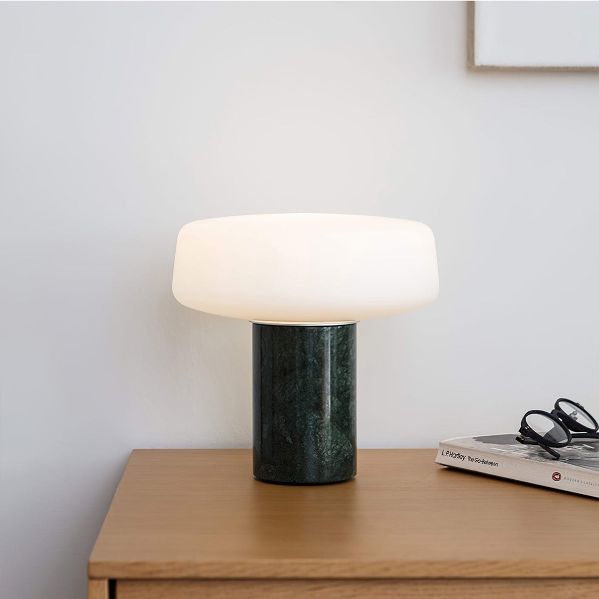 Green marble Clérachic table lamp lit on a wooden dresser corner, reading glasses resting on a stack of books.
