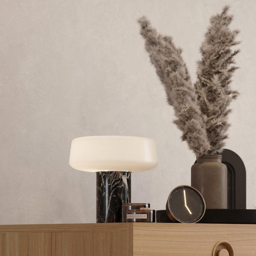 Dried pampas grass fills a vase beside a small clock and a black marble Clérachic table lamp lit on the dresser.