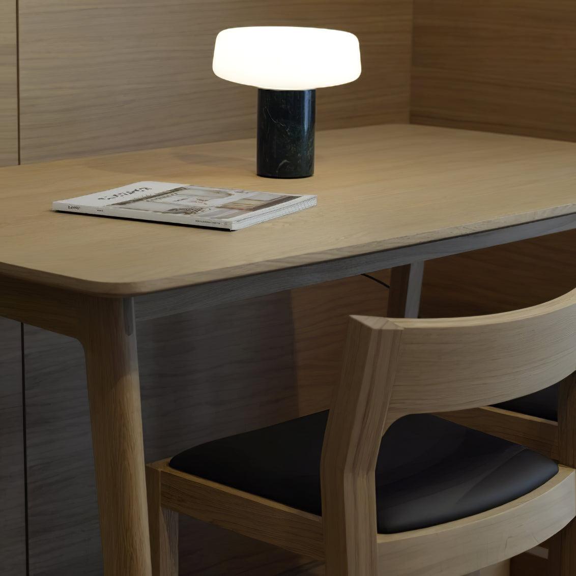 An open magazine lies on the desk beside a wooden chair and a black marble Clérachic table lamp lit nearby.