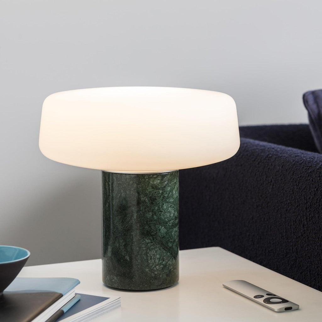 A small blue bowl and remote lie beside a green marble Clérachic table lamp lit near a navy sofa.