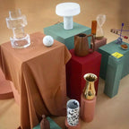 Vases and ceramics on coloured plinths surround a white marble Clérachic table lamp in this styled editorial scene.