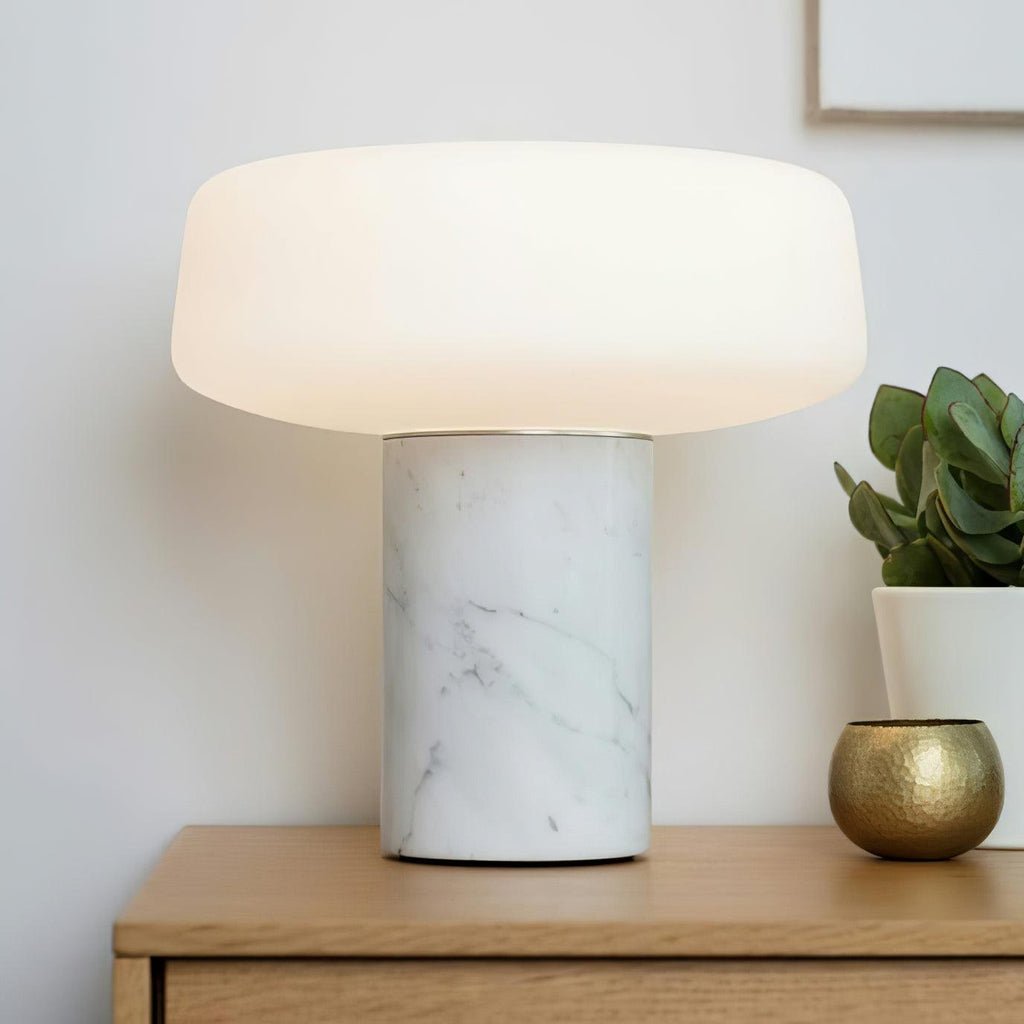A small potted plant and a brass ornament sit beside a white marble Clérachic table lamp on a wooden nightstand.