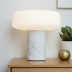 A small potted plant and a brass ornament sit beside a white marble Clérachic table lamp on a wooden nightstand.