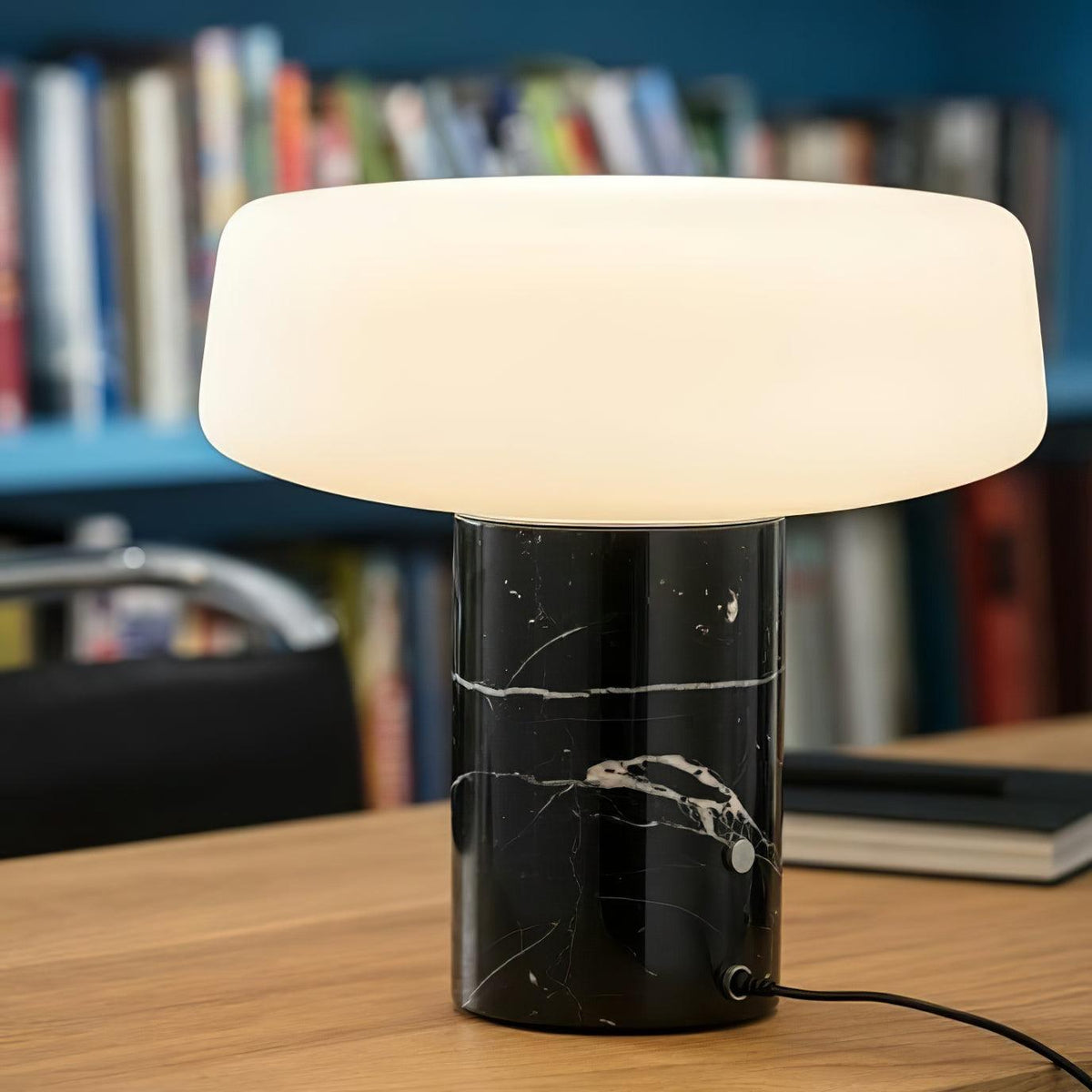 Black marble Clérachic table lamp with bold white veining, lit on a wooden table against a blue bookshelf.