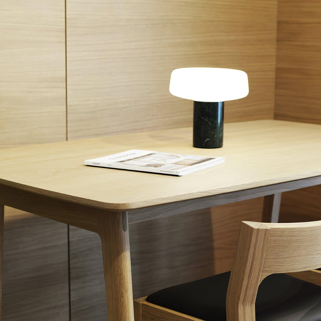 Dark marble Clérachic table lamp lit on a wooden desk with an open magazine, a wooden chair drawn up beside it.