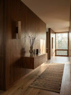 A floating console with a vase sits below this Clérachic wall light, lit, in a dark-panelled hallway.