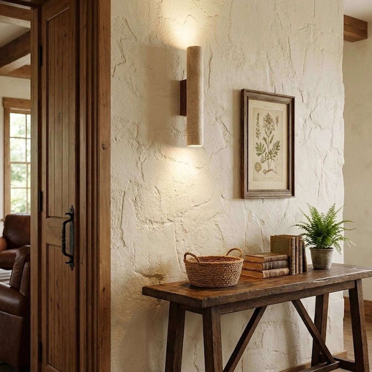 A framed botanical print hangs beside this Clérachic wall light, lit, on a textured plaster wall.