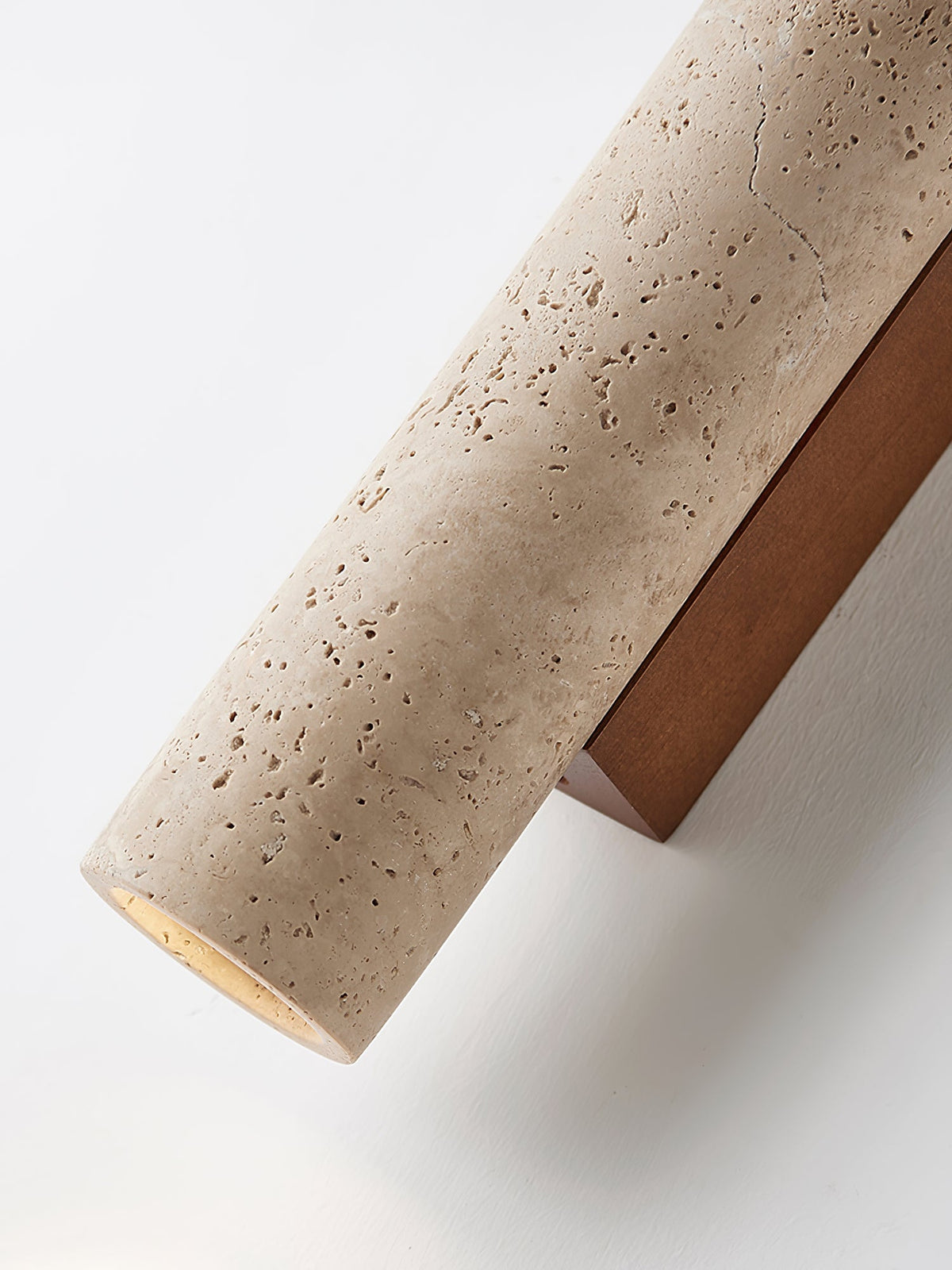 Close view of the pitted travertine texture on this Clérachic wall light, angled against the wall.