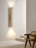 A rattan chair sits below this Clérachic wall light, lit, on a plaster wall beside a step.