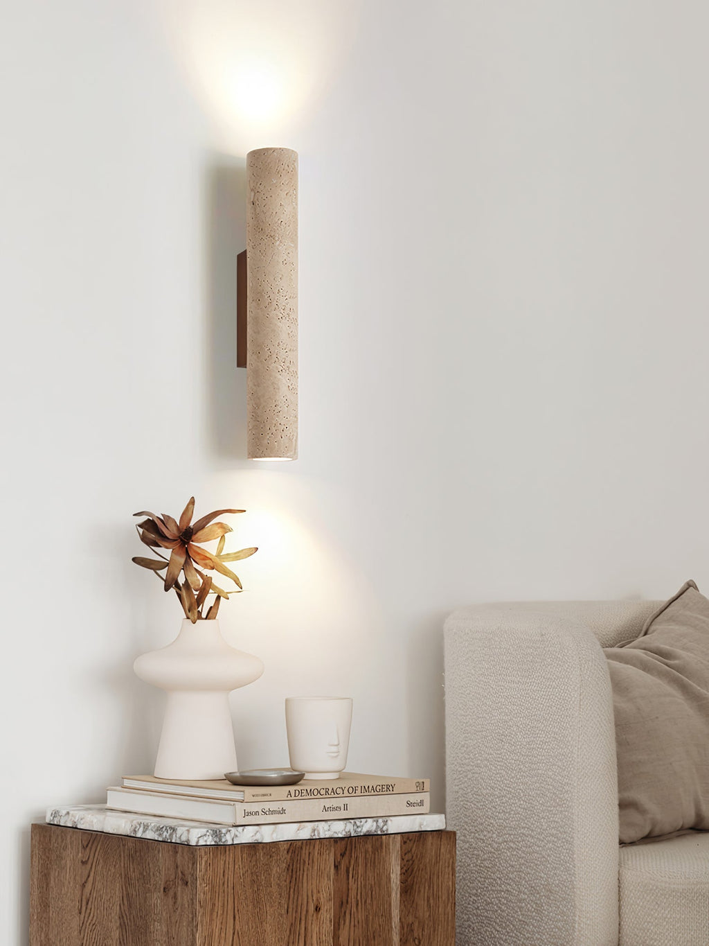 A side table with a sculptural vase and books sits below this Clérachic wall light, lit.